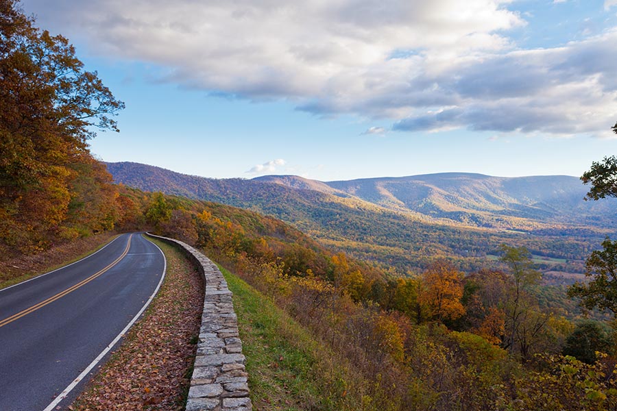 About Our Agency - a Winding Road Hugs the Edge of a Mountain Overlooking the Shenandoah Valley in Virginia, White Clouds Overhead and the Sun Shining on the Valley