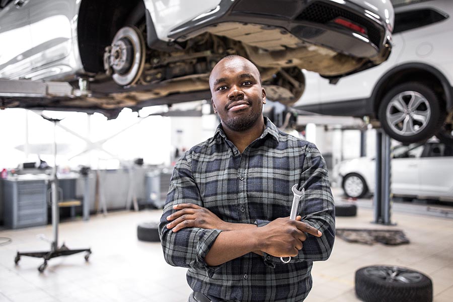 Business Insurance - an Auto Repair Garage Owner Stands Holding Tools, a Car Lifted Above Him