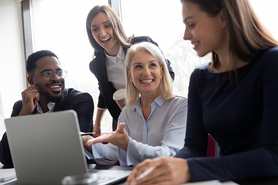 Employee Benefits - Group of Employees Laugh and Collaborate Over a Laptop at Work